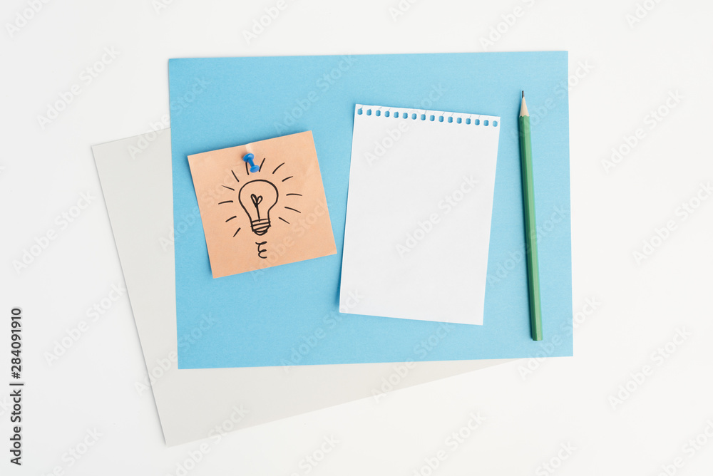 High angle view of drawn light bulb on sticky note attached with pushpin over white background High angle view of drawn light bulb on sticky note attached with pushpin over white background