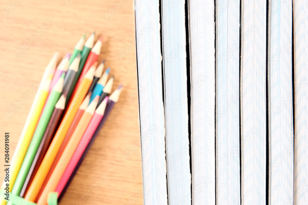 Obraz premium A stack of inverted shared notebooks on a table next to a blurred focus colored pencils. Brown table background.The concept of preparation for school