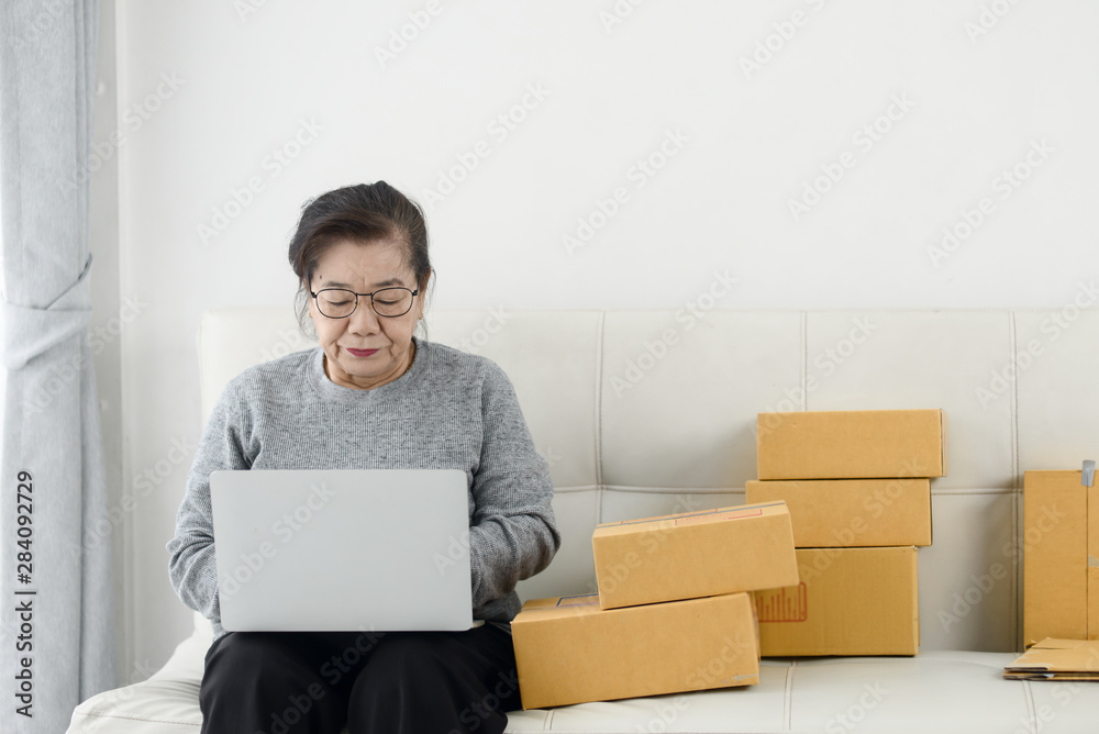 Asian senior woman using laptop while selling online with packaging, work at home concept. Asian senior woman using laptop while selling online with packaging, work at home concept.