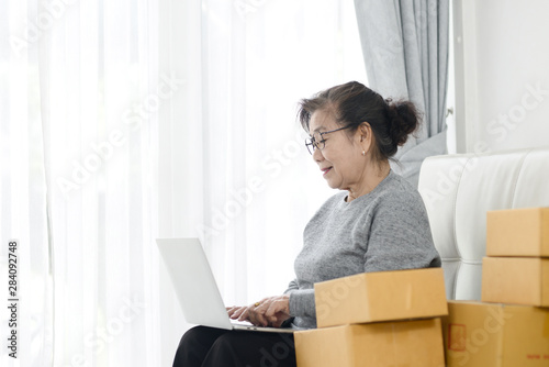 Asian senior woman using laptop while selling online with packaging, work at home concept. © nuiiko
