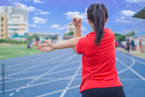 Young woman stretching her arms before running and exercising on running tracks. Young woman warming up outdoors. Sport and exercise concept.