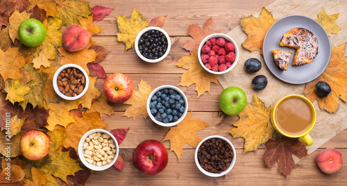 Seasonal autumn background. Frame of maple leaves and a cake  berries  raisins  apples  fruits  coffee and nuts over wooden background.