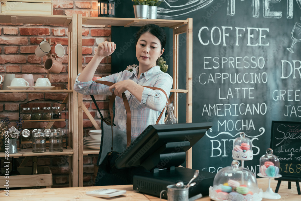 early morning female barista open cafe store and begin good day wearing on professional apron in wood counter. asian woman coffee shop owner put on denim apron and start to work in coffeehouse.