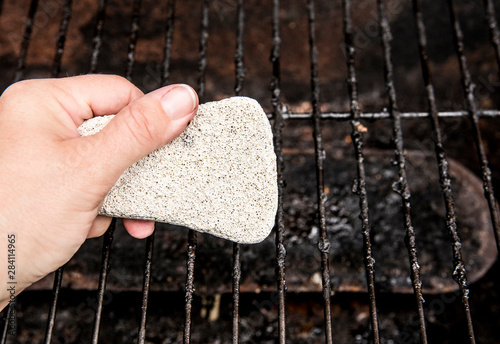 Hand holding and using natural pumice stone to scrub charred food deposits and rust from BBQ grill metal grid. Safe way to clean grill concept. photo