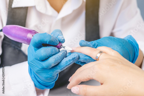 Female manicurist doing manicure hardware cutter removing old varnish in the salon. Concept of professional nail care