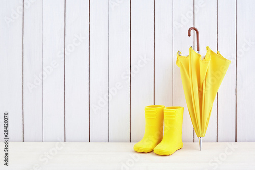 A pair of yellow rain boots and a umbrella on white wooden background © vetre
