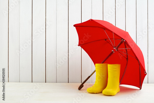 Photography A pair of yellow rain boots and a umbrella on white wooden background