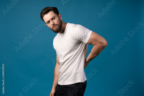 Young male suffering from back pain against a blue background. Portrait of a handsome man. Concept- backpain, spine problems.