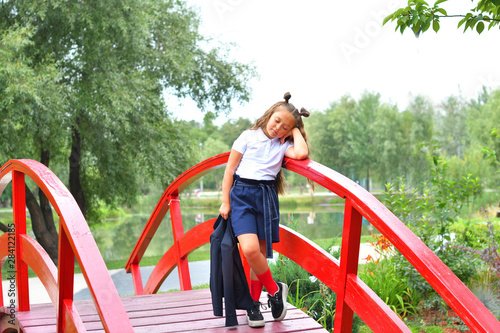 Portrait of a beautiful young Schoolgirl on the background park and red bridge