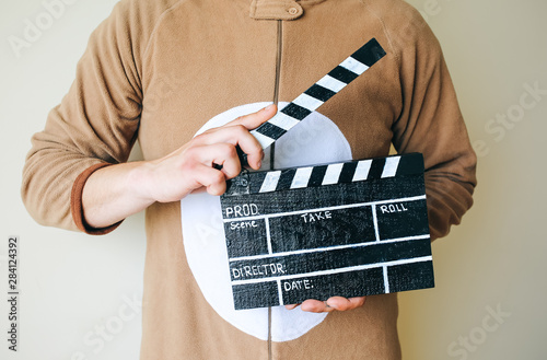 Man in cosplay costume holding black clapperboard. Guy in the funny animal pyjamas sleepwear making a film. Directing and of amateur cinema movie. Creative concept. Japanese anime. photo