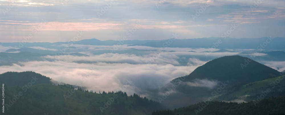 Amazing sunrise in the mountains. Great view of the foggy valley with bright sun rays in Carpathians. Impressive mountain landscape with rising sun and rugged mountains raise above the clouds.