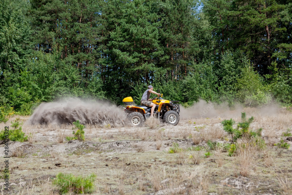Man riding a yellow quad ATV all terrain vehicle on a sandy forest. Extreme sport motion, adventure, tourist attraction. Man riding a yellow quad ATV all terrain vehicle on a sandy forest. Extreme sport motion, adventure, tourist attraction.