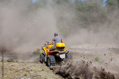 Man riding a yellow quad ATV all terrain vehicle on a sandy forest. Extreme sport motion, adventure, tourist attraction.