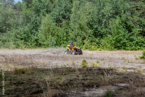 Man riding a yellow quad ATV all terrain vehicle on a sandy forest. Extreme sport motion, adventure, tourist attraction.