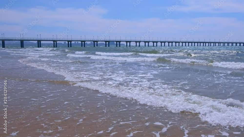 Beautiful coastal town at seaside. View on sea with waves and pier, coastal city and mountains on background at sunny day.