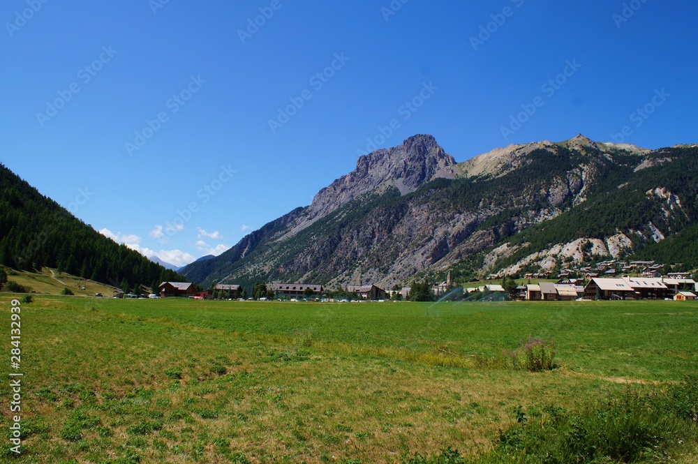 Mountain pastures in the national parc Queras in French alps, and the village of Ceyac at the foot of a summit