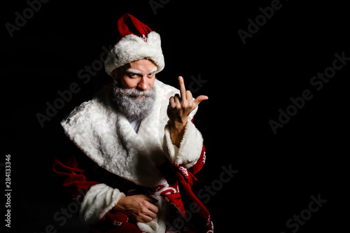 Portrait of a bad brutal mature Santa Claus showing middle finger signs, isolated on black background