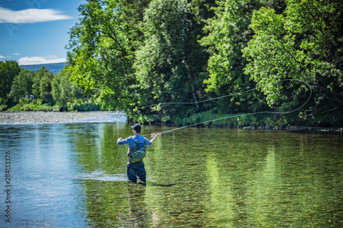 Angler mit Angel in Wathose im Fluss beim Fliegenfischen bei Sonne