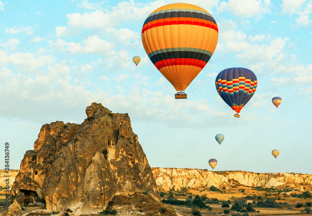 Colorful air balloons fly up into the sky at sunrise among a beautiful rocky landscape. Cappadocia Turkey.