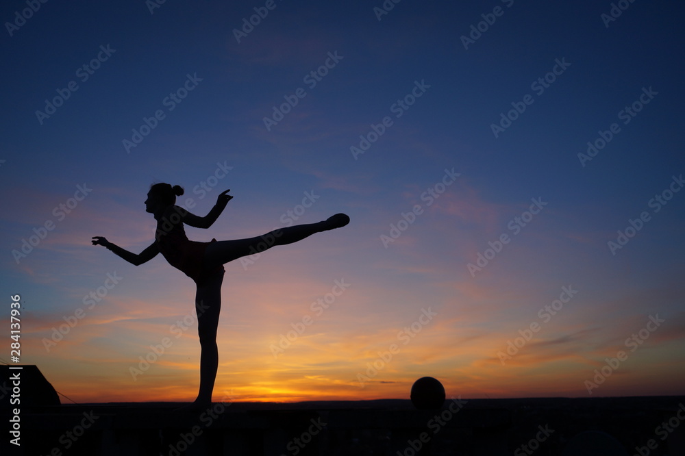 dancer in the dance does the splits in the air against the sunset