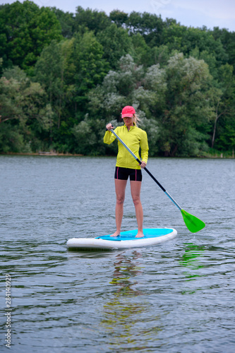 Sporty girl rowing on a SUP board on a big river and enjoy life. Stand on the paddle boarding house - amazing outdoor activities. Side view.