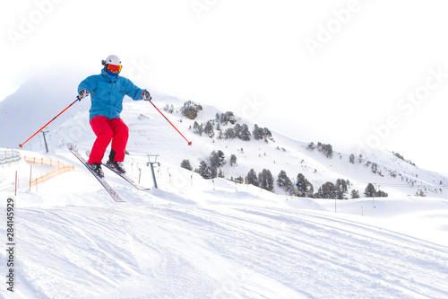 Skier man with orange ski glasses in white helmet make release jump on ski slope on top in Alps mountains. On the background of mountains. Close up view.