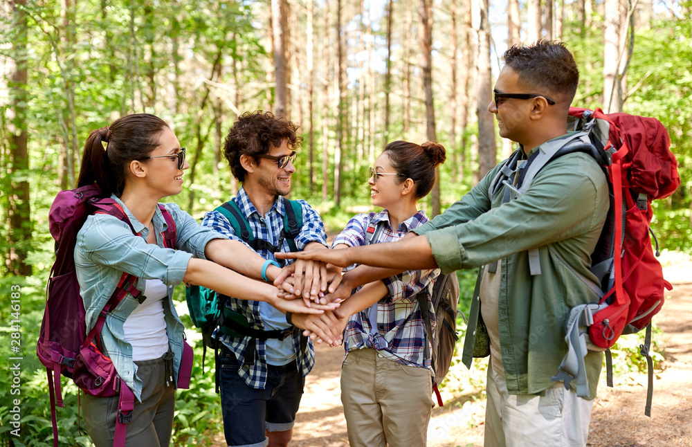 travel, tourism, hike and friendship concept - group of friends with backpacks stacking hands in forest travel, tourism, hike and friendship concept - group of friends with backpacks stacking hands in forest
