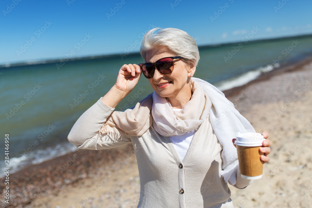 people and leisure concept - senior woman in sunglasses drinking takeaway coffee on beach in estonia people and leisure concept - senior woman in sunglasses drinking takeaway coffee on beach in estonia