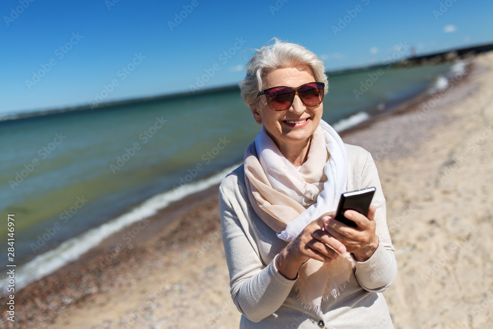 old people and leisure concept - happy smiling senior woman using smartphone on beach in estonia