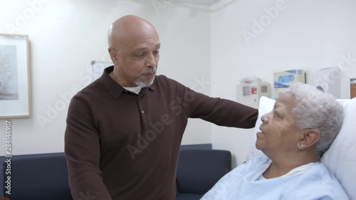 Elderly female hospital patient in patient gown holds hands with husband photo