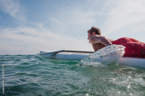 Teenage boy lying on a surfboard paddling out to sea, Laguna Beach, California, United States