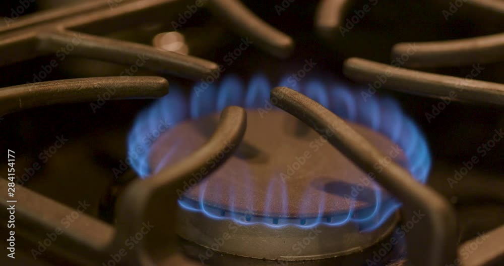 A close up of a gas stove burner igniting and the classic blue flame