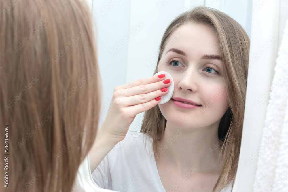 Reflection of a young girl in the mirror, removes makeup with cotton pad Reflection of a young girl in the mirror, removes makeup with cotton pad