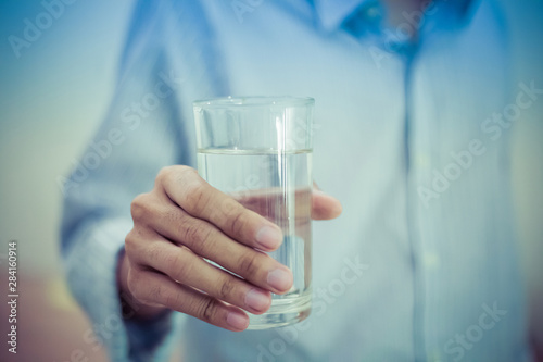 Closeup young man holding drinking water glass in him hand. Health care concept. photo