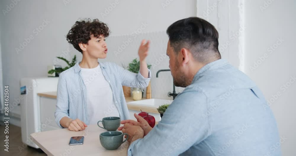 Unhappy wife beautiful young lady is fighting with sad husband during breakfast in kitchen talking gesturing discussing problems. People and relationship concept. Unhappy wife beautiful young lady is fighting with sad husband during breakfast in kitchen talking gesturing discussing problems. People and relationship concept.