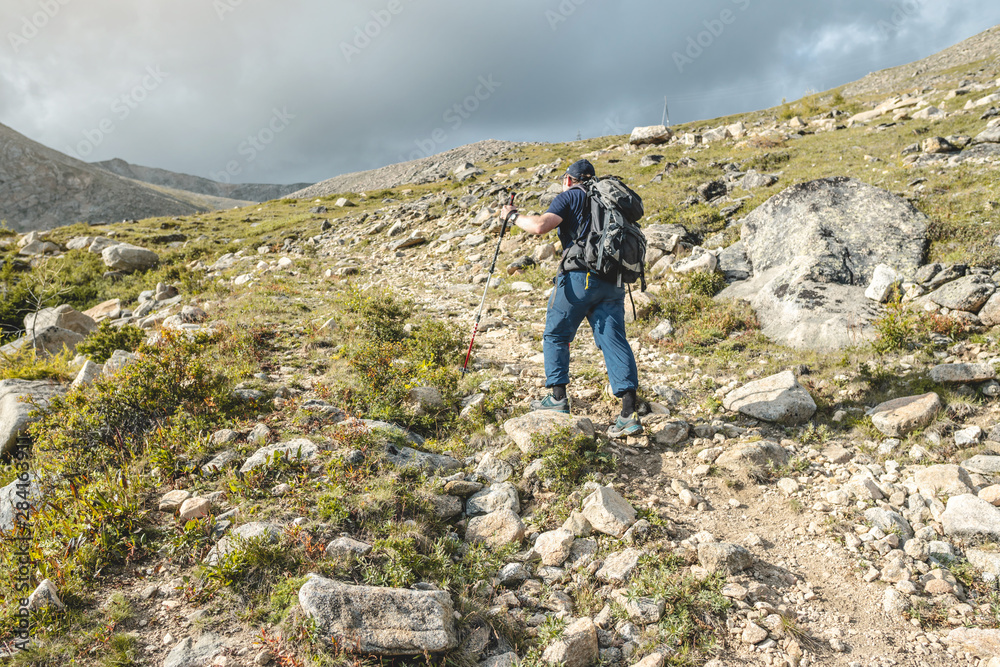 Man Hiking with backpack during the ascent of the peak in the summer. Concept trekking trips and active life with nature