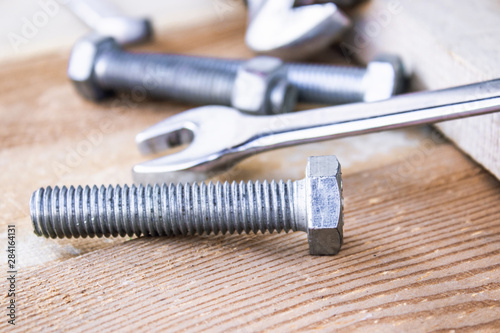 Steel bolts and nuts lie on wooden boards next to an adjustable wrench.