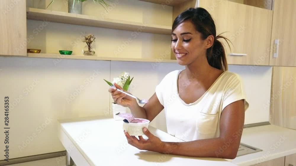 Beautiful fit woman enjoying while eating yogurt for a light snack at the home.