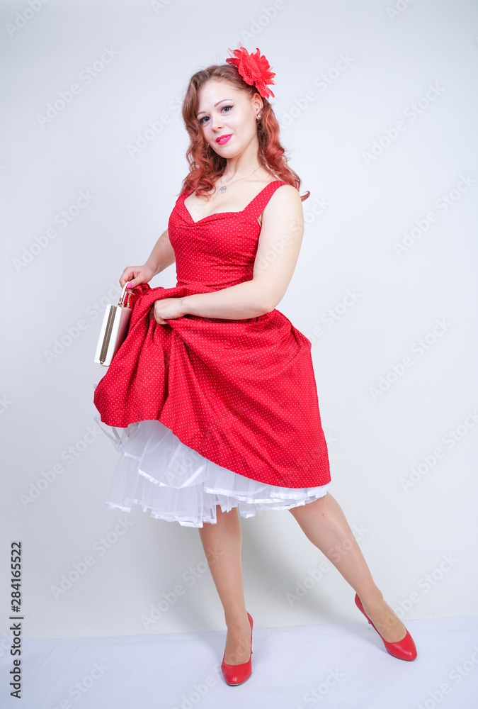 Beautiful redheaded girl in red midi pinup style dress isolated on white studio background standing alone Beautiful redheaded girl in red midi pinup style dress isolated on white studio background standing alone