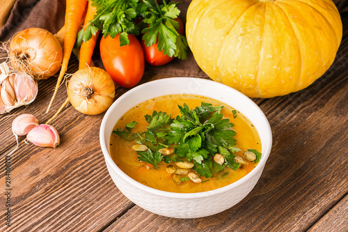 Pumpkin and fresh vegetables soup in white bowl wooden background. Natural rustic style. Vertical frame. Autumn concept.