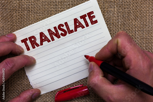 Writing note showing Translate. Business photo showcasing Another word with same equivalent meaning of a target language Man's hand hold white paper with symbolic letter jute sack background photo