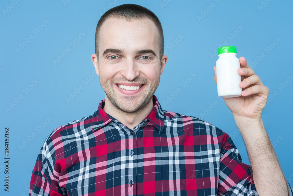 Attractive man shows a container of medicine, copy space, advertising, text, close up, blue background Attractive man shows a container of medicine, copy space, advertising, text, close up, blue background