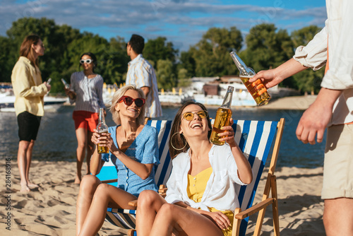 young, cheerful multicultural men and women drinking beer while resting on beach
