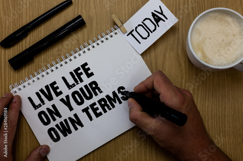 Text sign showing Live Life On Your Own Terms. Conceptual photo Give yourself guidelines for a good living Paperclip retain written notepad hand hold marker coffee black pen on woody desk photo