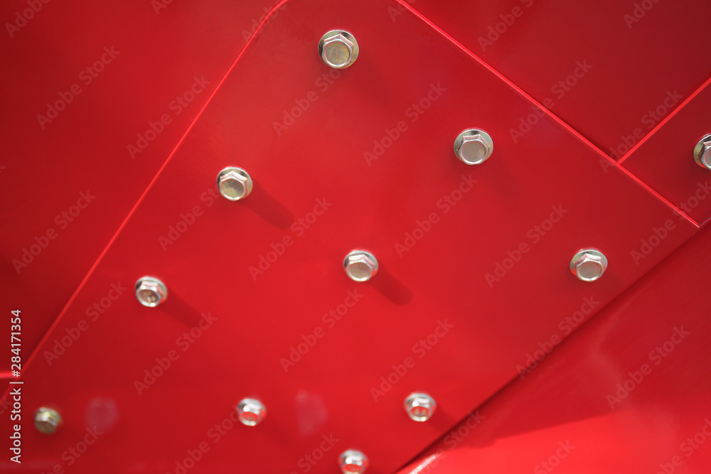 Fototapeta Zbliżenie śrub i nakrętek na żelaznej ścianie pomalowanej na czerwono