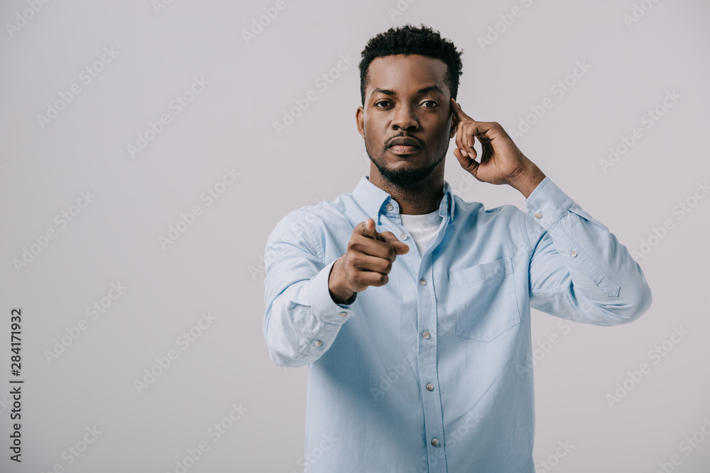 selective focus of handsome african american man touching temple and pointing with finger isolated on grey selective focus of handsome african american man touching temple and pointing with finger isolated on grey