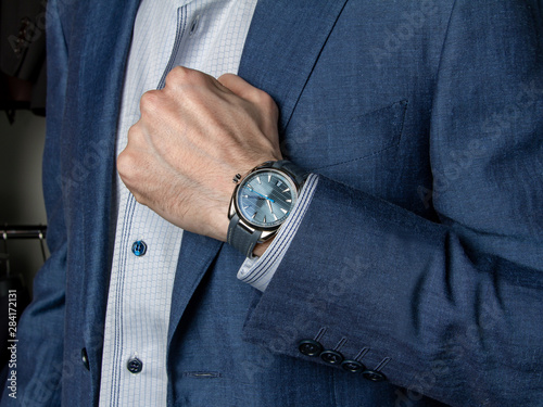 A man in a classic suit shows an expensive wristwatch
