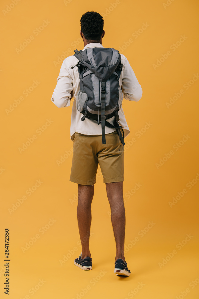 Fototapeta premium back view of african american man standing with backpack on orange