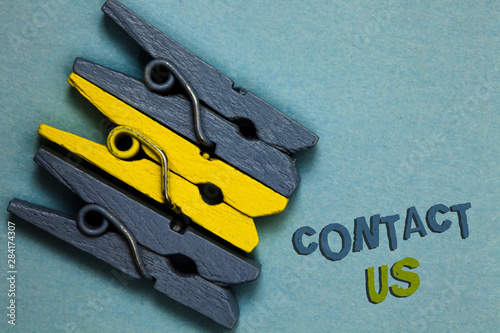 Conceptual hand writing showing Contact Us. Business photo text Group of person that rendering costumer service through telecom Gray yellow vintage clothespins clear background Holding things photo