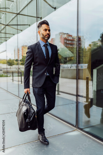 Young Indian Businessman Walking By Office Windows . Reflection photo